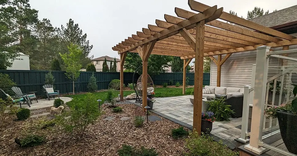 Wooden pergola over patio with furniture and dog in backyard.