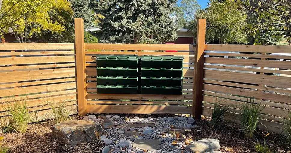 Green planting pockets on wooden fence with gravel and rocks.
