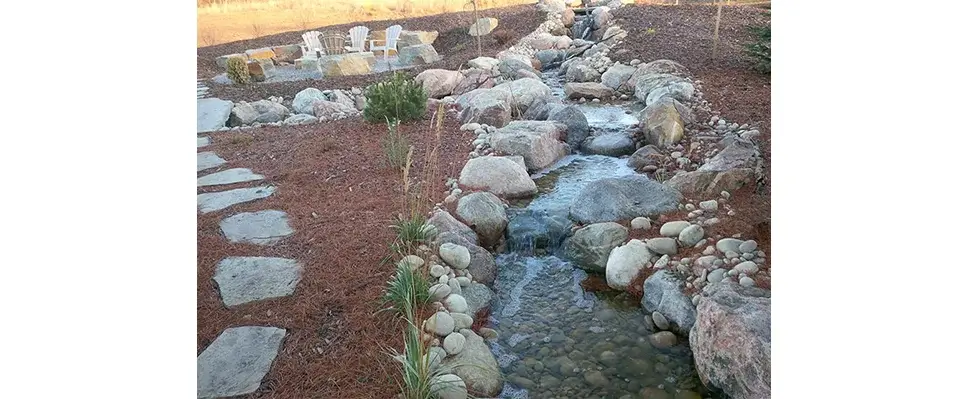 Natural backyard landscape design featuring a recirculating rock stream and seating area.