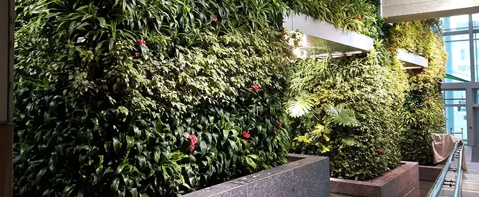 Lush indoor living wall with tropical plants and red flowers in a modern commercial lobby.