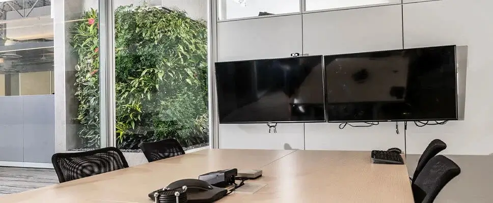 Modern conference room in Edmonton with wooden table, dual monitors, glass wall, and lush indoor green wall.