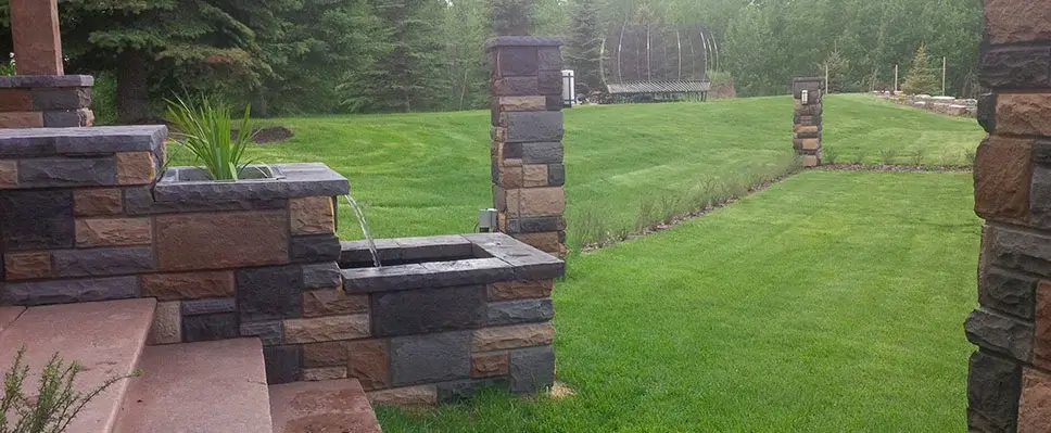 A professionally constructed natural stone waterfall and stream feature with artistic rock placement and surrounding mulch in an Edmonton backyard.