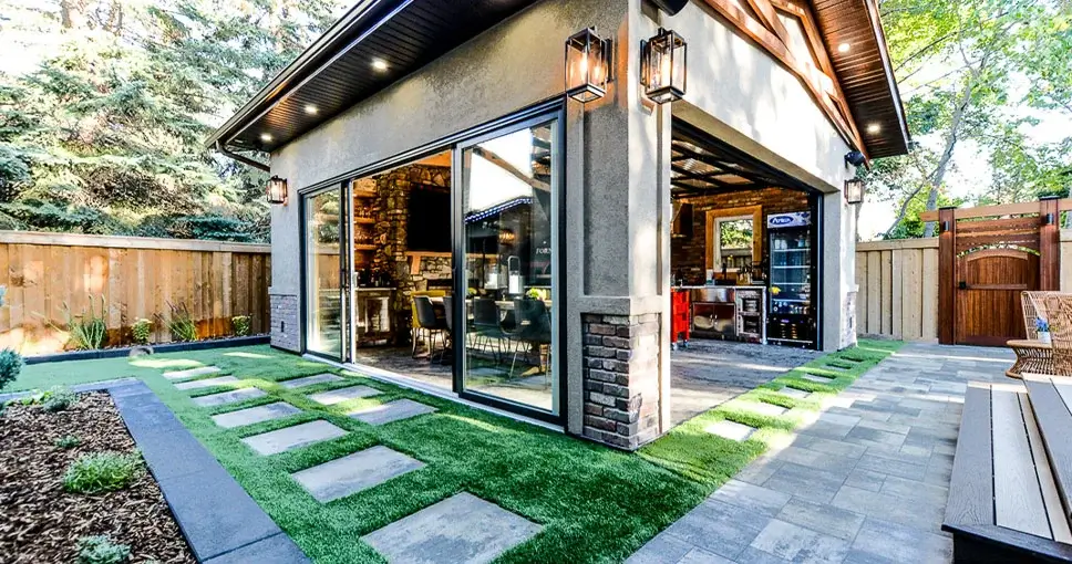 Modern backyard with a stylish outdoor kitchen, glass sliding doors, and a landscaped walkway.