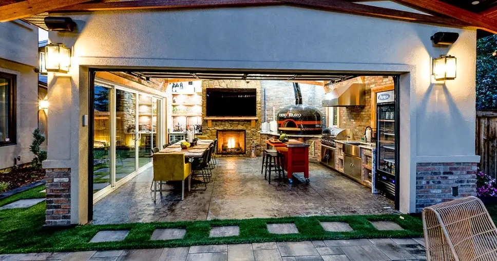 Luxury outdoor kitchen and dining space with a fireplace, pizza oven, and modern appliances.