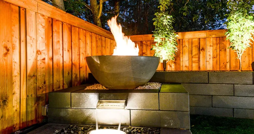 Modern fire bowl with cascading water feature in a landscaped backyard.