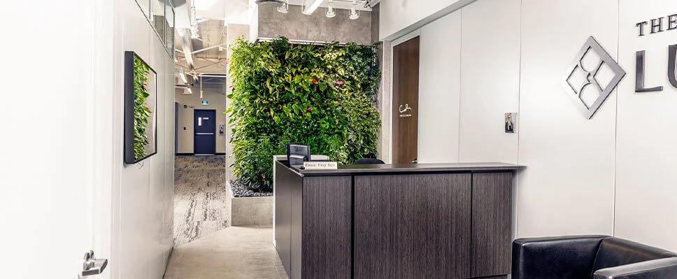Edmonton office reception with vertical green wall, dark wood desk, and consultation door.