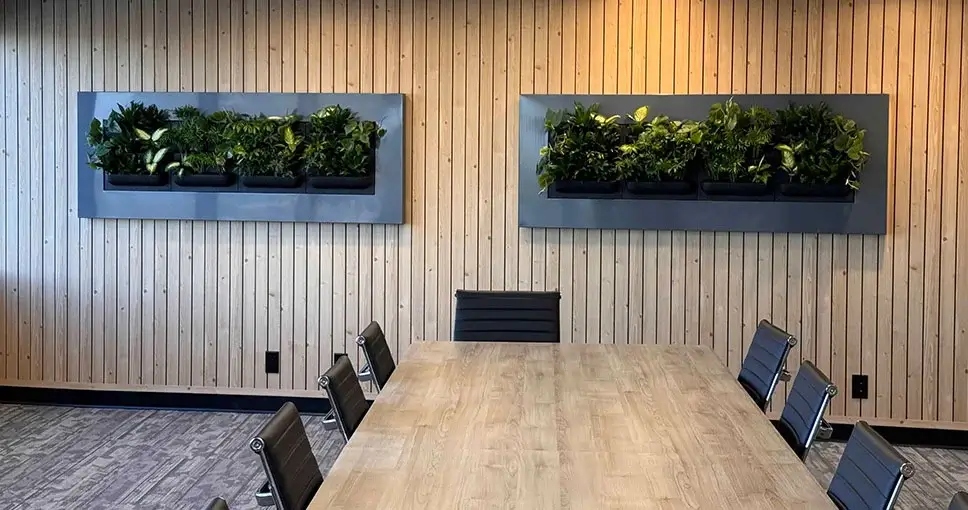Two indoor vertical gardens on wooden wall above conference table.