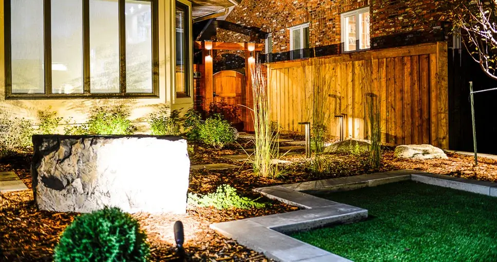 Beautifully landscaped backyard with modern lighting and a natural stone feature.