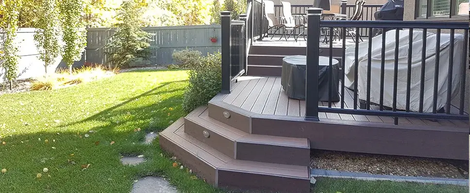 A multi-level brown composite deck featuring black railings and integrated LED step lighting in an Edmonton backyard.