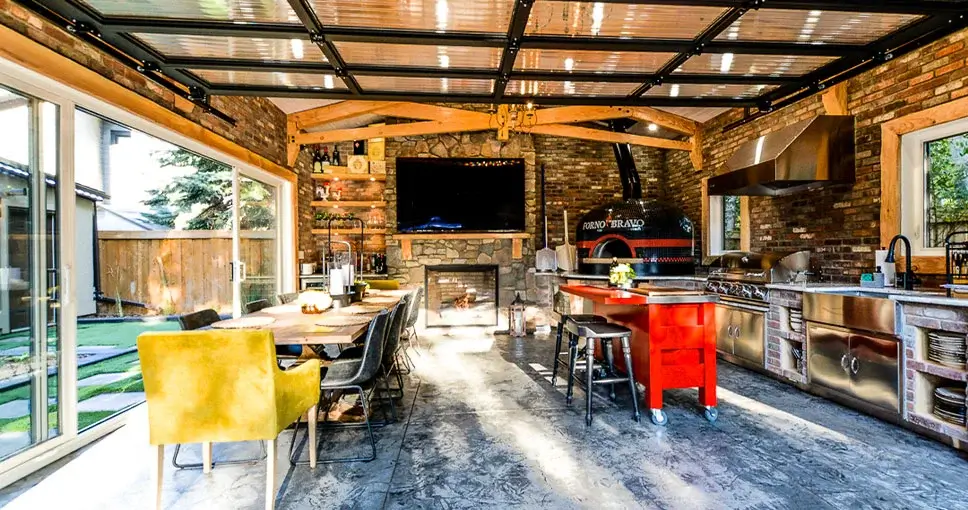 Stylish outdoor kitchen and dining area with a fireplace, wood-fired pizza oven, and modern appliances.