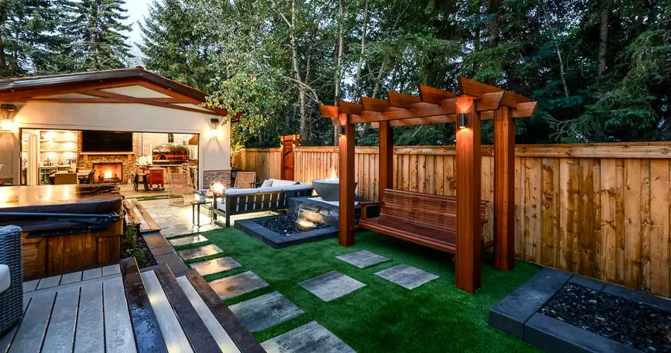 A luxury backyard featuring a wooden pergola with a bench, a fire pit, and a modern outdoor kitchen area.