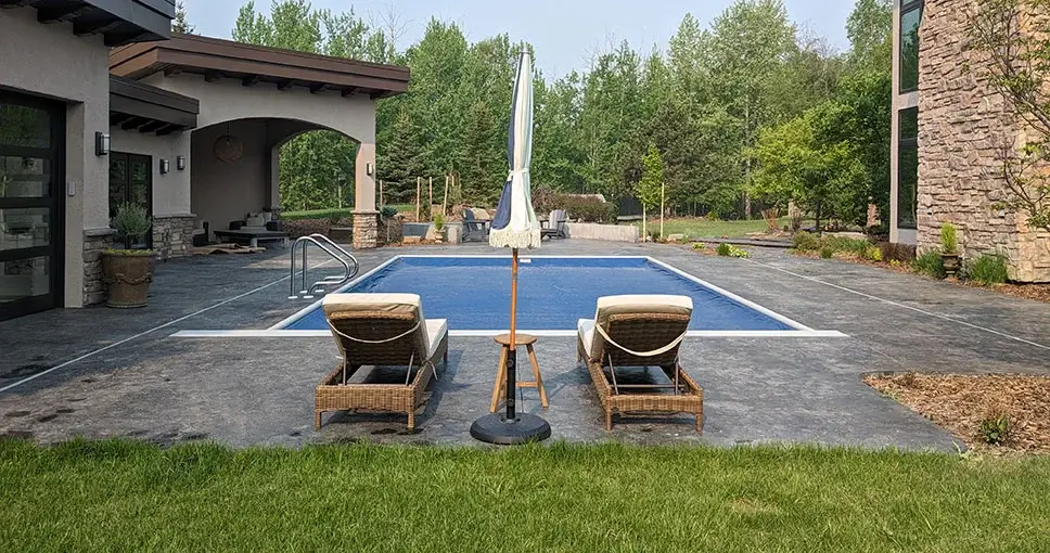 Poolside lounge chairs with an umbrella facing a covered pool.