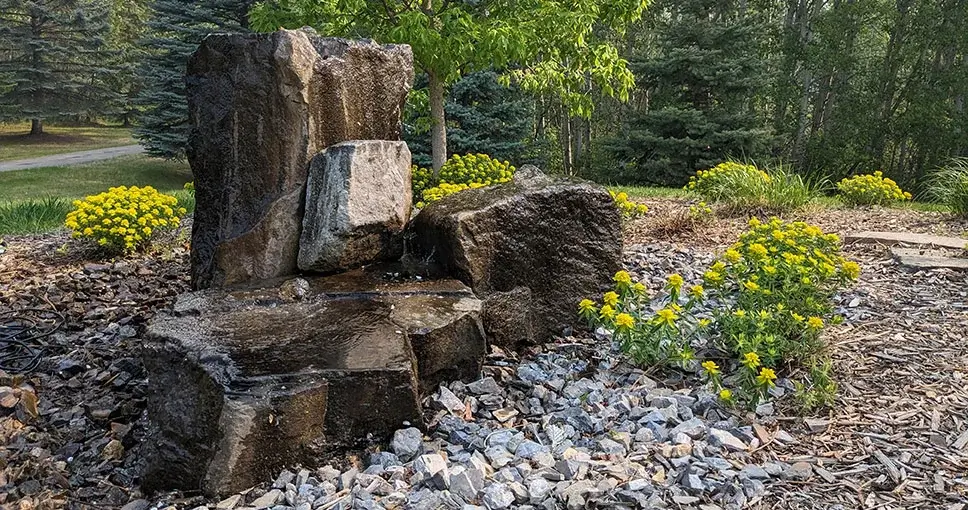 Stone water feature with yellow flowers in garden.