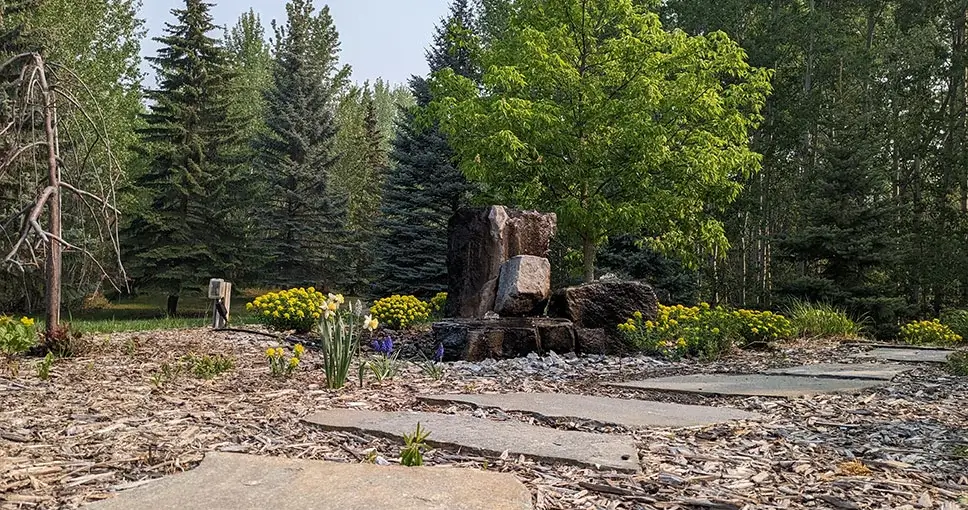 Garden with stone water feature, pathway, and trees.