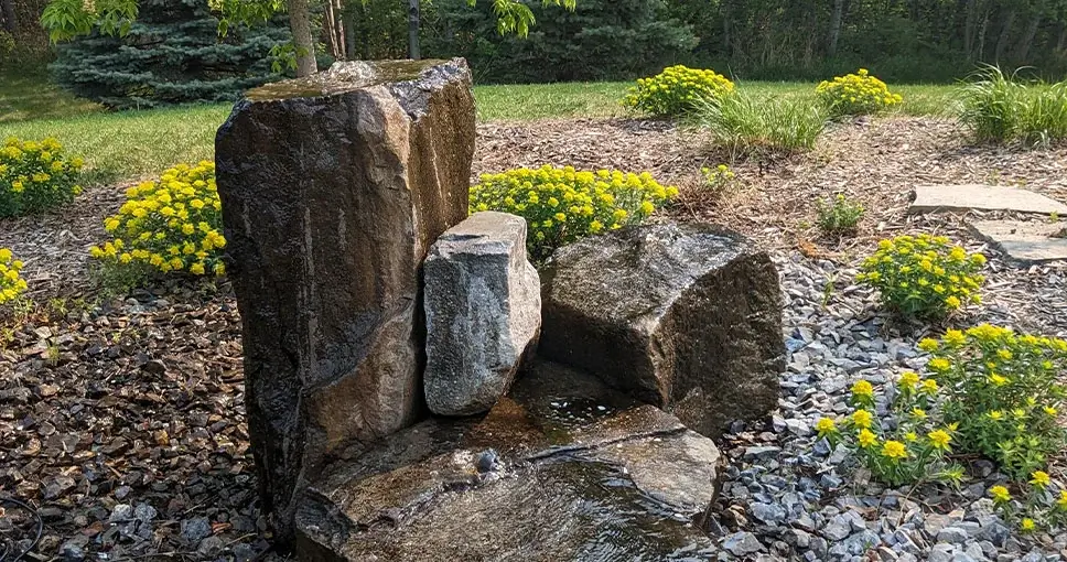 Stone water feature in garden with yellow flowers.