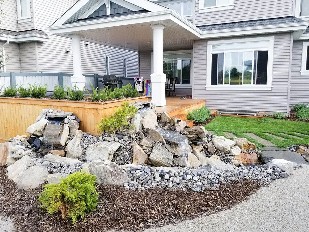Front yard landscape in Edmonton with decorative rock waterfall, mulch beds, shrubs, & covered porch.
