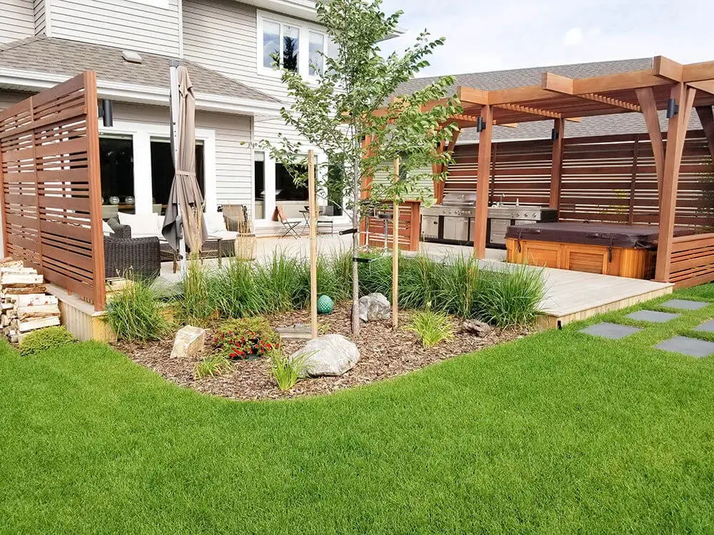 Backyard landscaping in Edmonton with pergola, hot tub, outdoor kitchen, seating area, & ornamental garden bed.