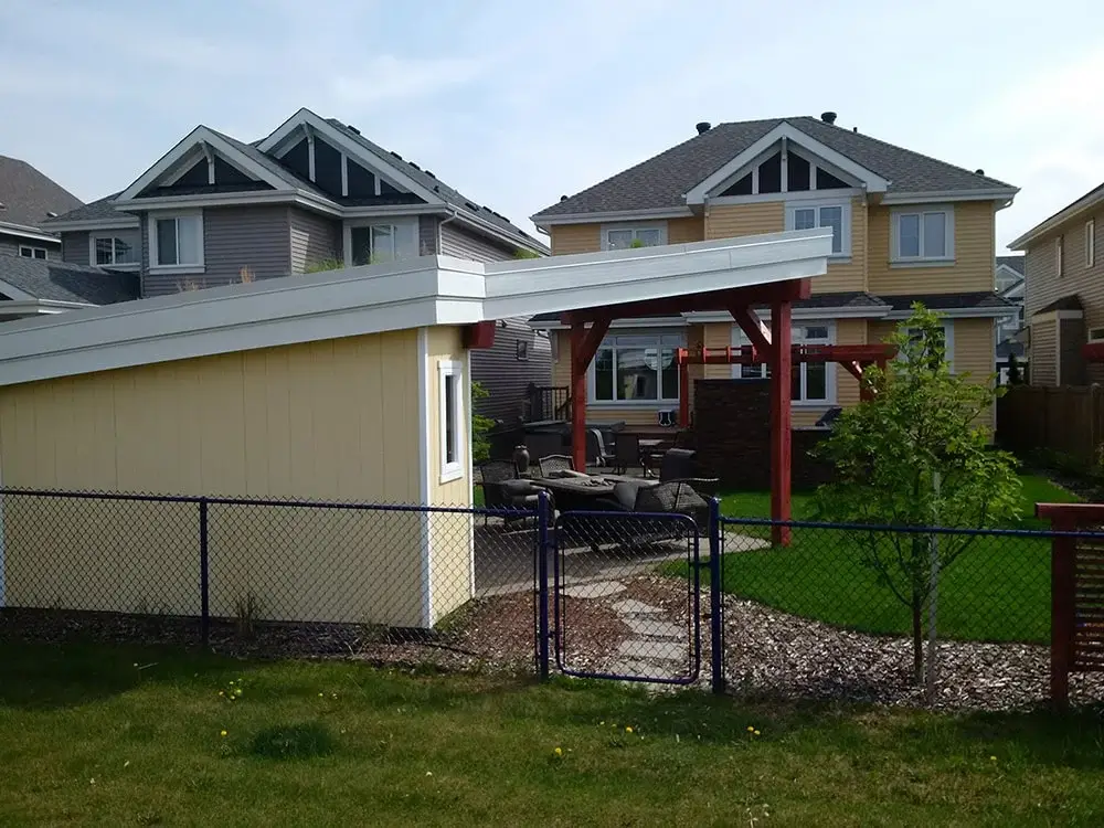 Suburban backyard in Edmonton with patio furniture, yellow shed, pergola, stone path, and landscaped lawn.
