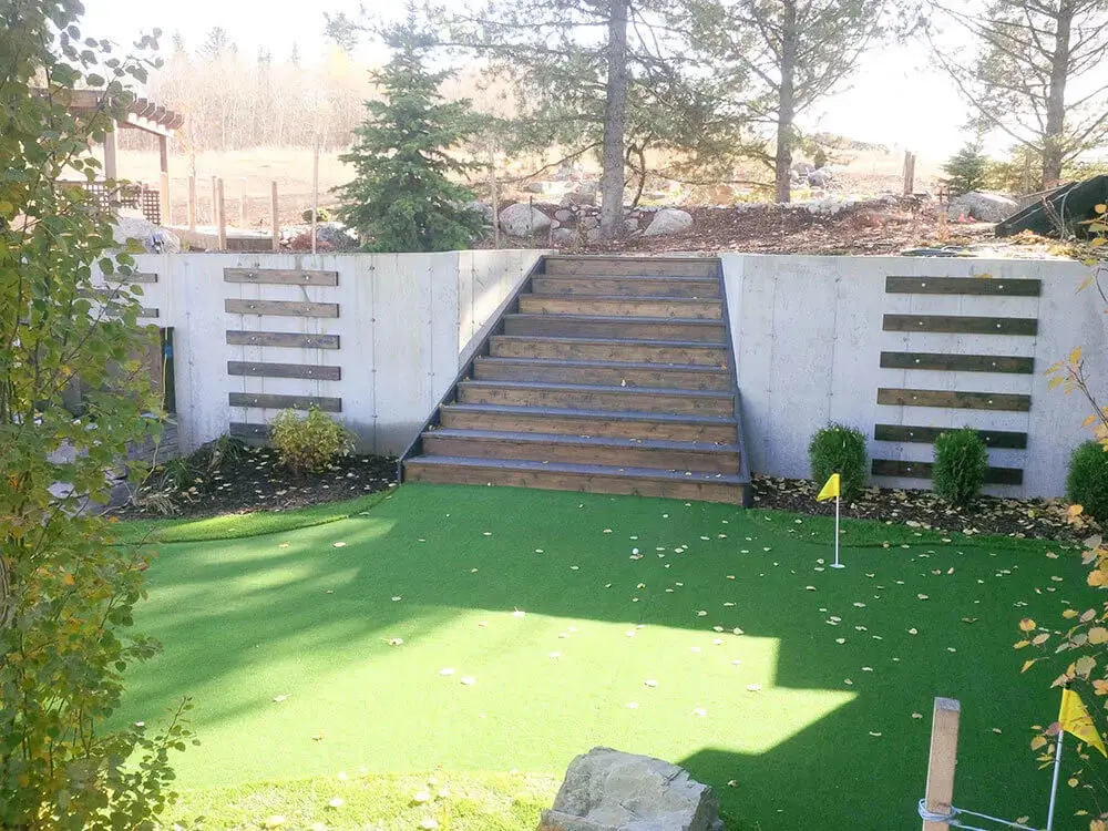 Backyard landscaping in Edmonton with artificial putting green, wooden retaining wall, and staircase to upper yard.