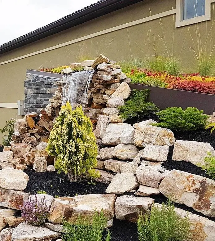Sloped garden with stone waterfall, plants, and retaining wall—part of custom landscape construction by Terra in Edmonton
