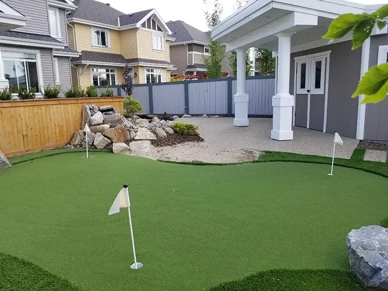 Professional backyard putting green with synthetic turf, flags, and a rock water feature next to a shed.