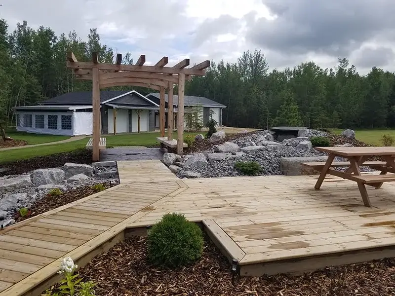Large wooden ground-level deck with a matching pergola and stone landscaping.