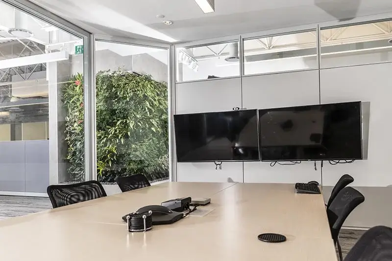 A clean office meeting room with glass walls overlooking a lush indoor living wall.