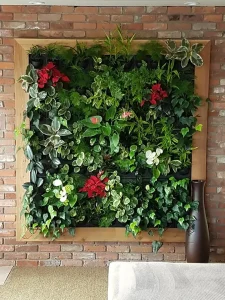 A lush, square vertical living wall with a light wood frame featuring diverse plants like Poinsettias and Ivy, mounted on a red brick wall.