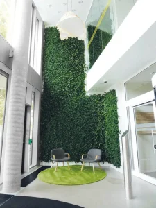 A massive vertical living wall stretching up a high-ceiling atrium behind a modern seating area with two grey chairs.
