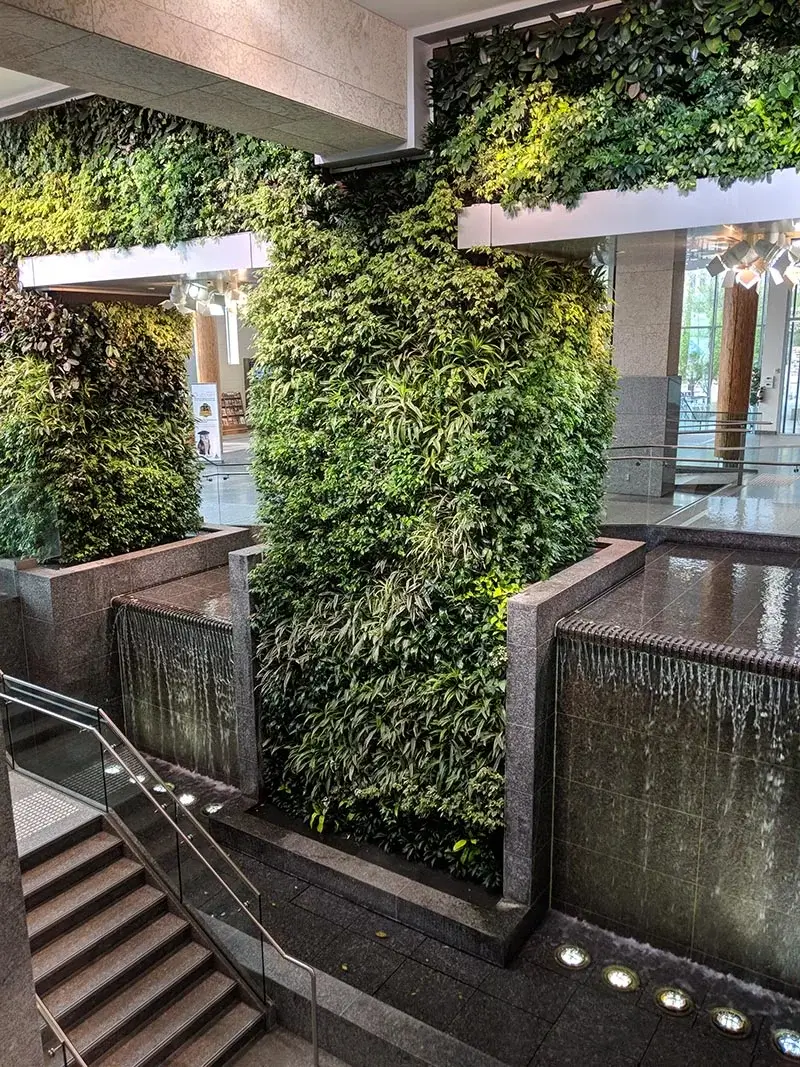 A lush indoor vertical garden wall positioned between two modern stone waterfalls in a bright atrium.