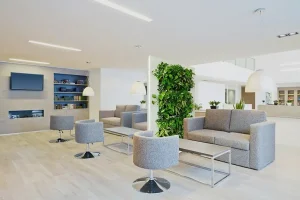 A bright, modern office lounge with grey sofas and a central free-standing vertical living wall divider.