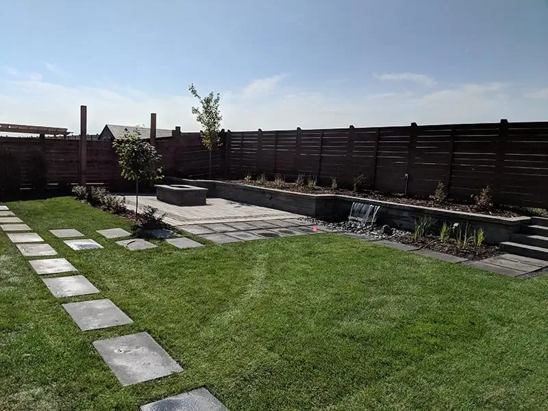 Modern backyard featuring a stone fire pit, paver patio, and a retaining wall with a built-in waterfall.
