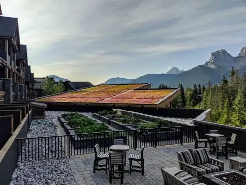 Sloped green roof panels and patio seating with a mountain backdrop.
