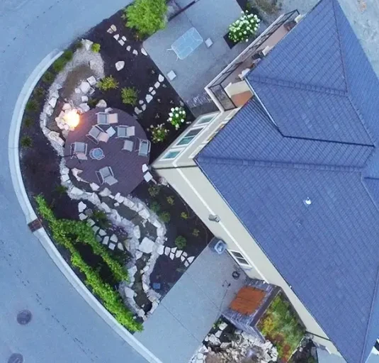 Top-down aerial view of a residential lot with a circular deck, fire pit, and curved stone pathways.