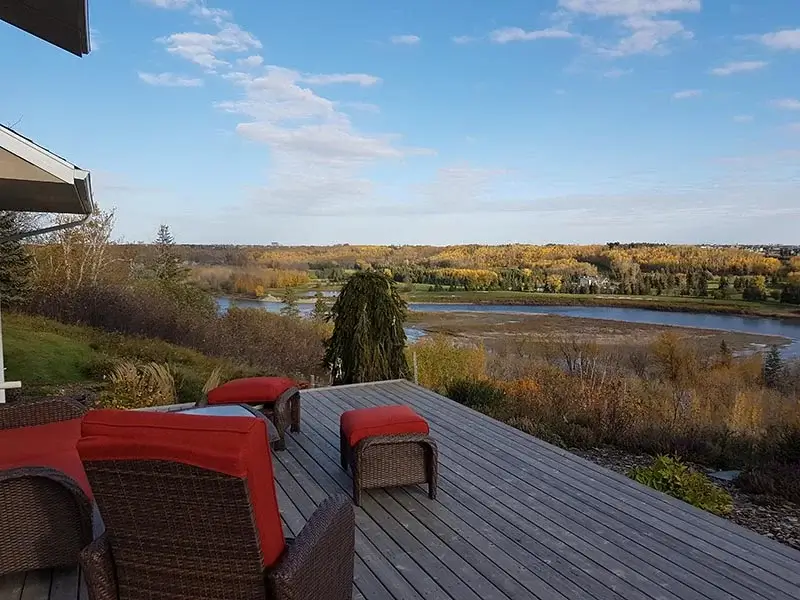 Grey composite deck with red cushion chairs overlooking a river and autumn forest.