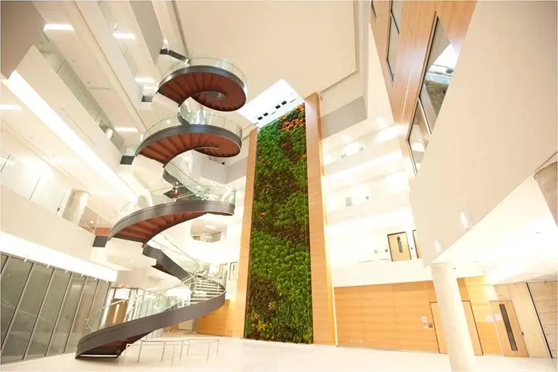 A modern multi-story atrium featuring a dramatic spiral staircase and a massive vertical living wall.