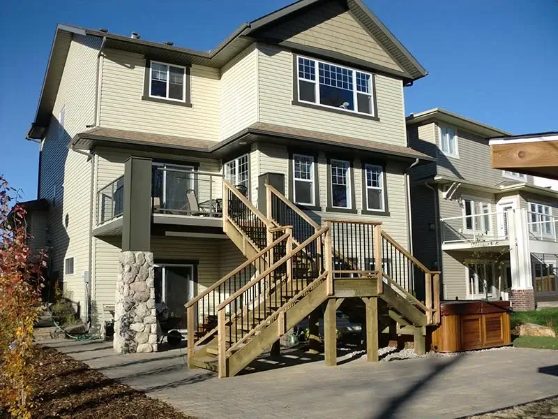 A large wooden staircase connecting a second-story balcony to a ground-level stone paver patio.