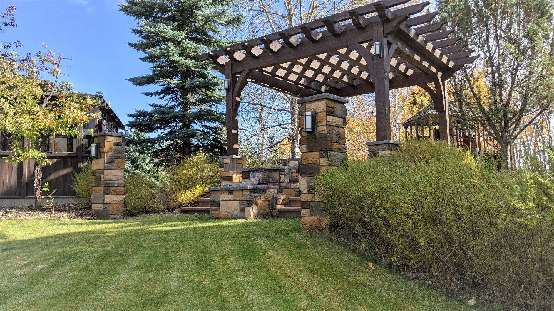 Dark wood pergola with stone pillars and a waterfall.