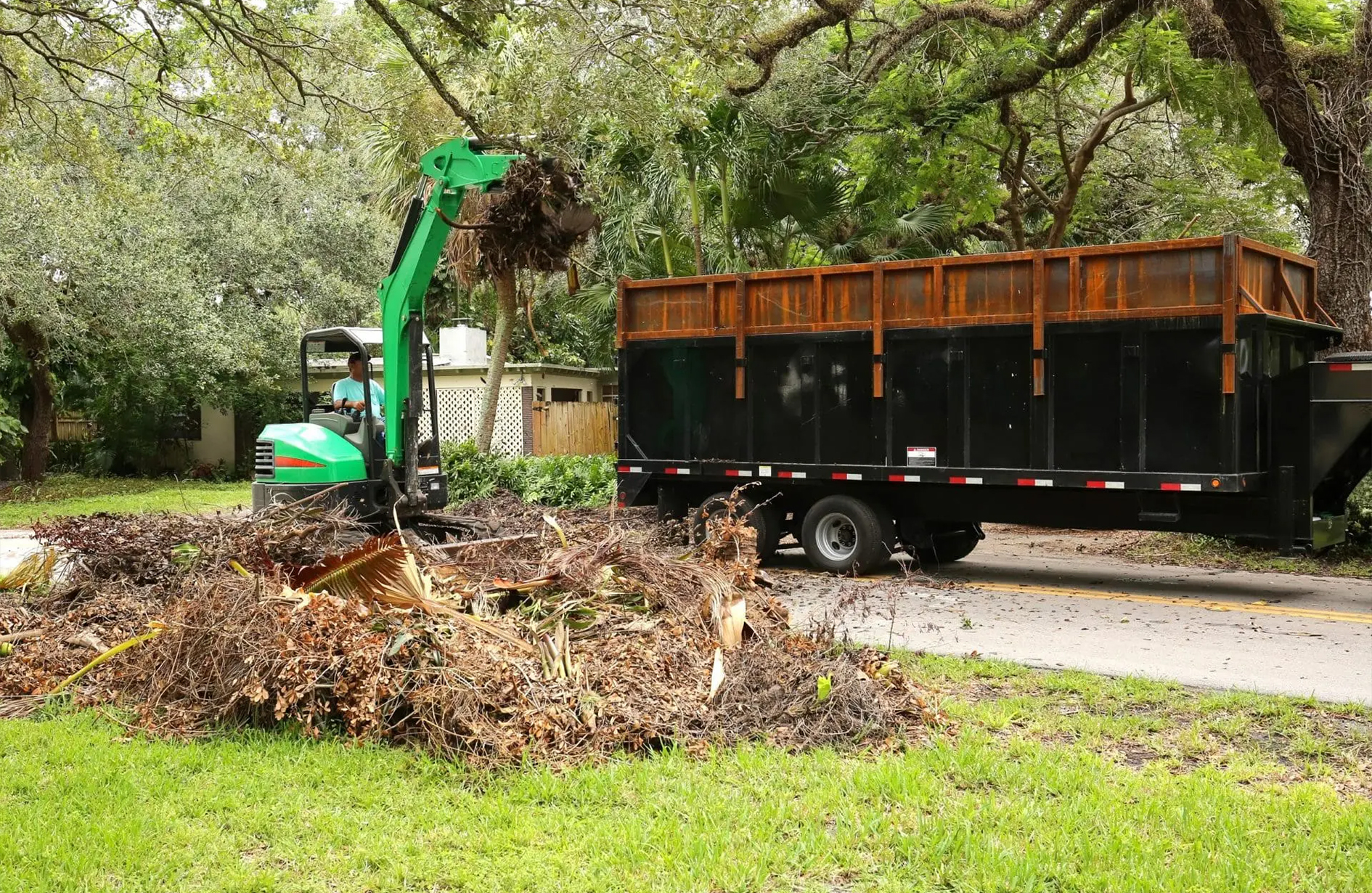 Spring clean up with mini excavator removing yard debris into dump trailer of garden area.