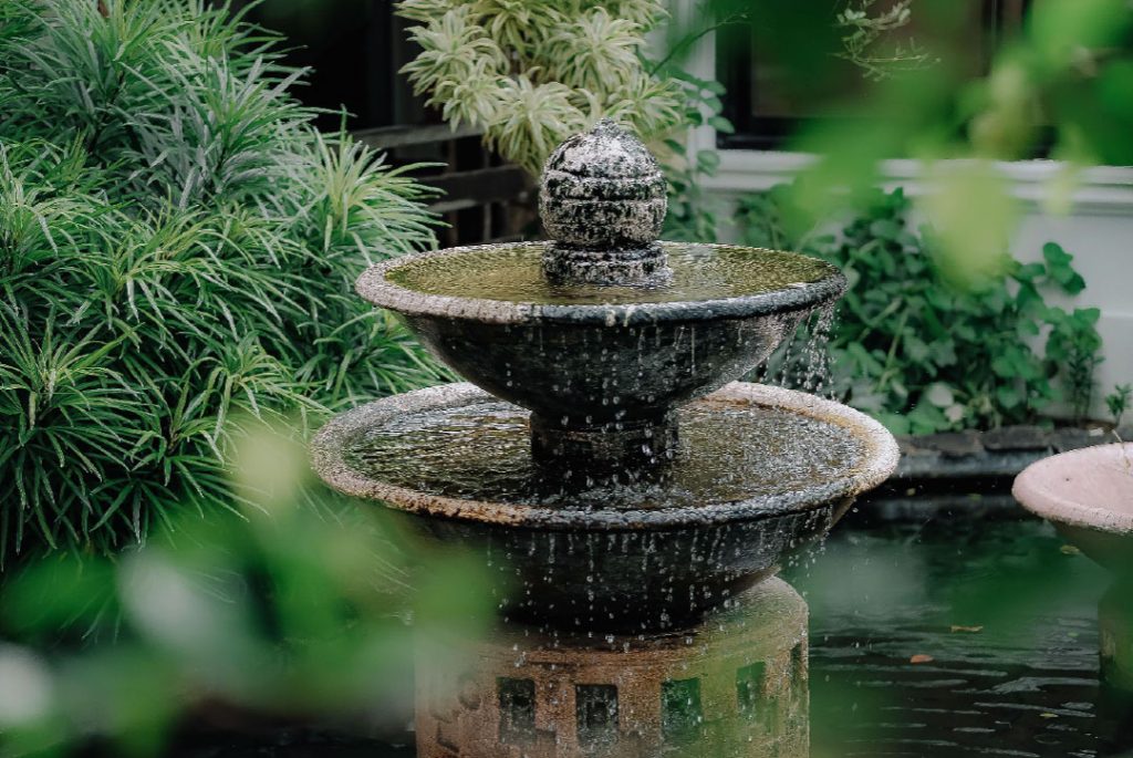 Tiered fountain with water flowing during spring clean up, surrounded by lush greenery.