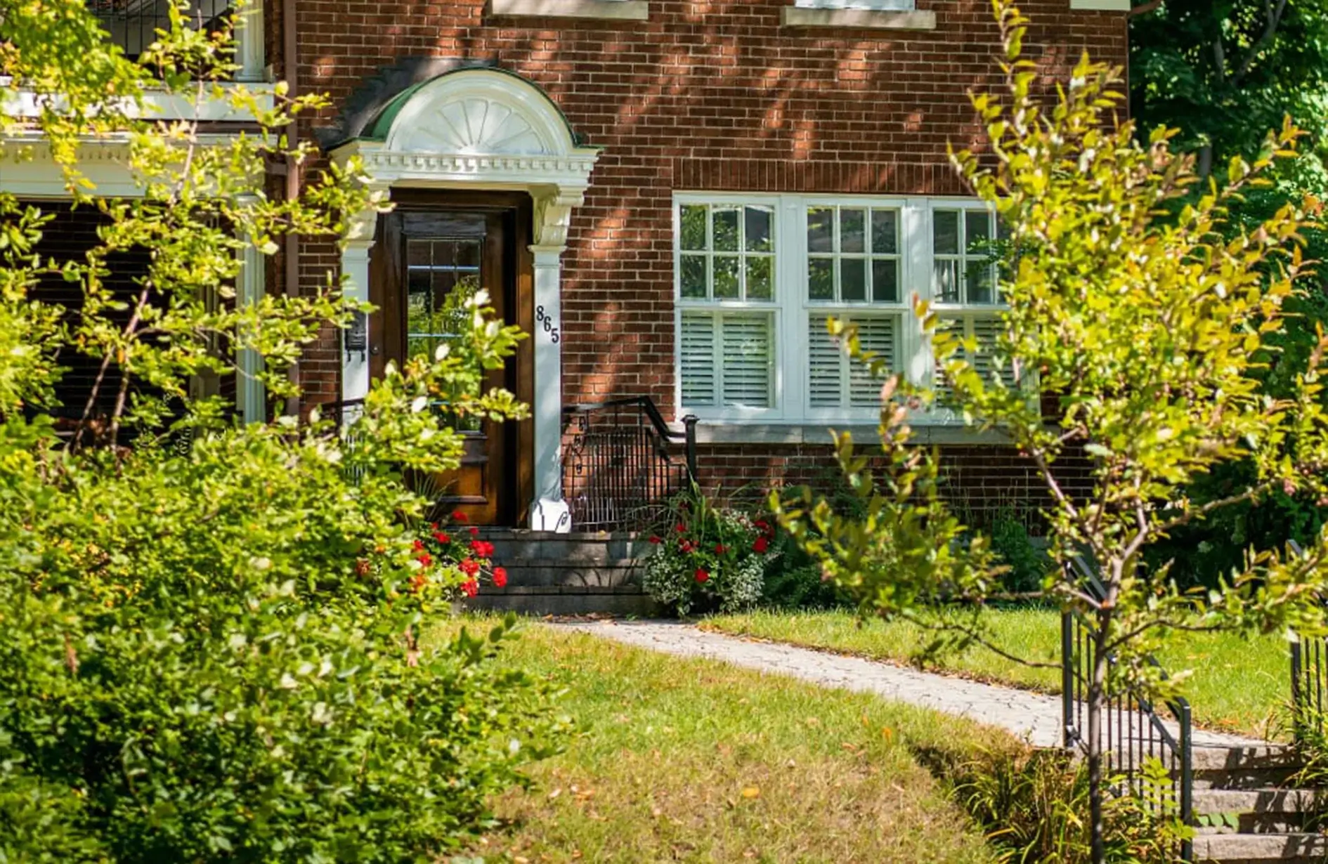 A brick house with a front door and windows, surrounded by green trees and a small lawn path.