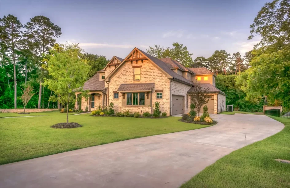 A large modern stone house featuring a clean concrete driveway and professional front yard landscaping.