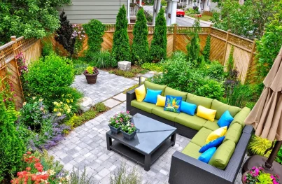 a well-designed small backyard patio, featuring a comfortable outdoor seating area with a sofa and coffee table, surrounded by lush greenery and a stone path.