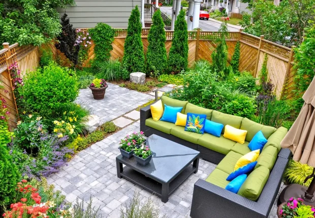 a well-designed small backyard patio, featuring a comfortable outdoor seating area with a sofa and coffee table, surrounded by lush greenery and a stone path.
