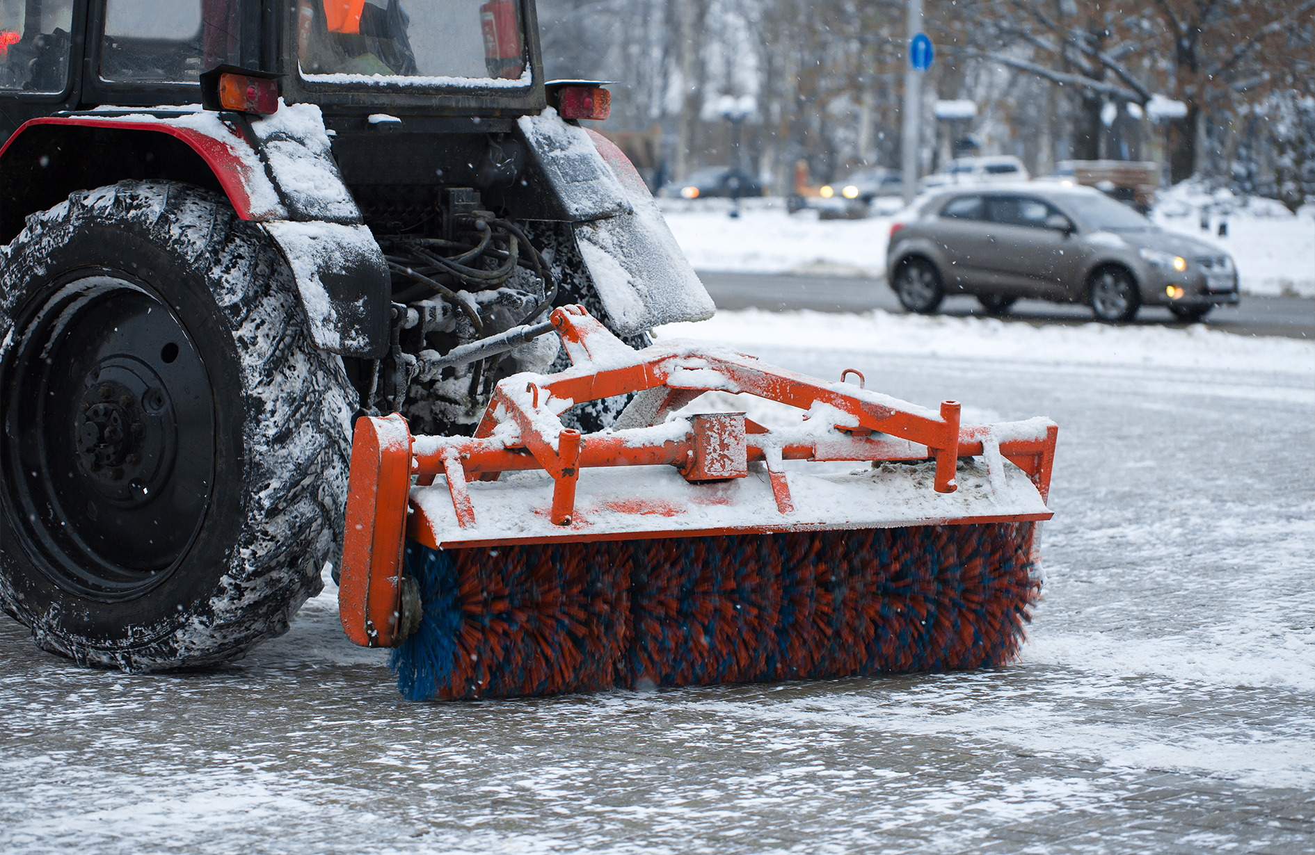 Snow removal Edmonton with rotating brush plow clearing urban road, surrounded by cars, trees, and winter conditions.