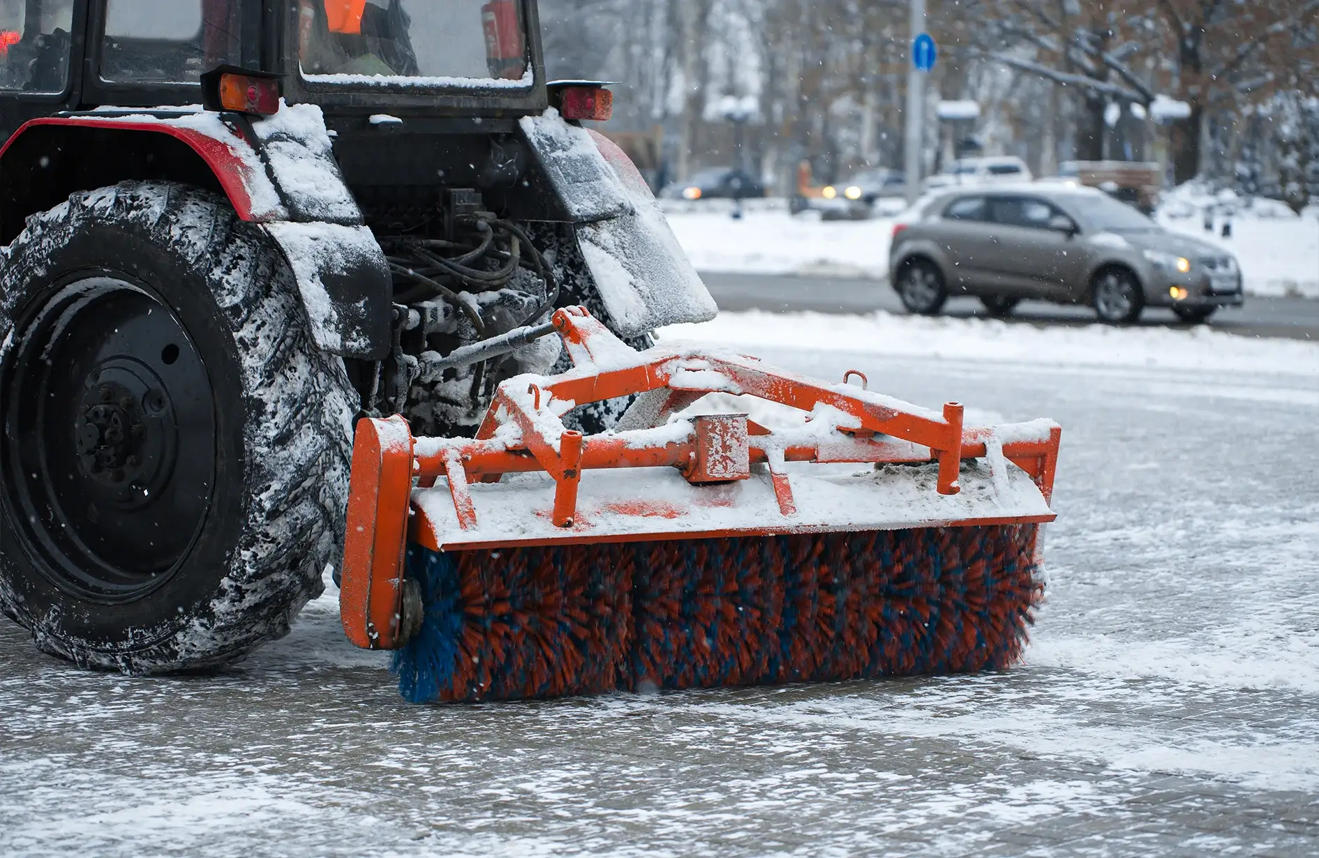 Snow removal Edmonton with rotating brush plow clearing urban road, surrounded by cars, trees, and winter conditions.