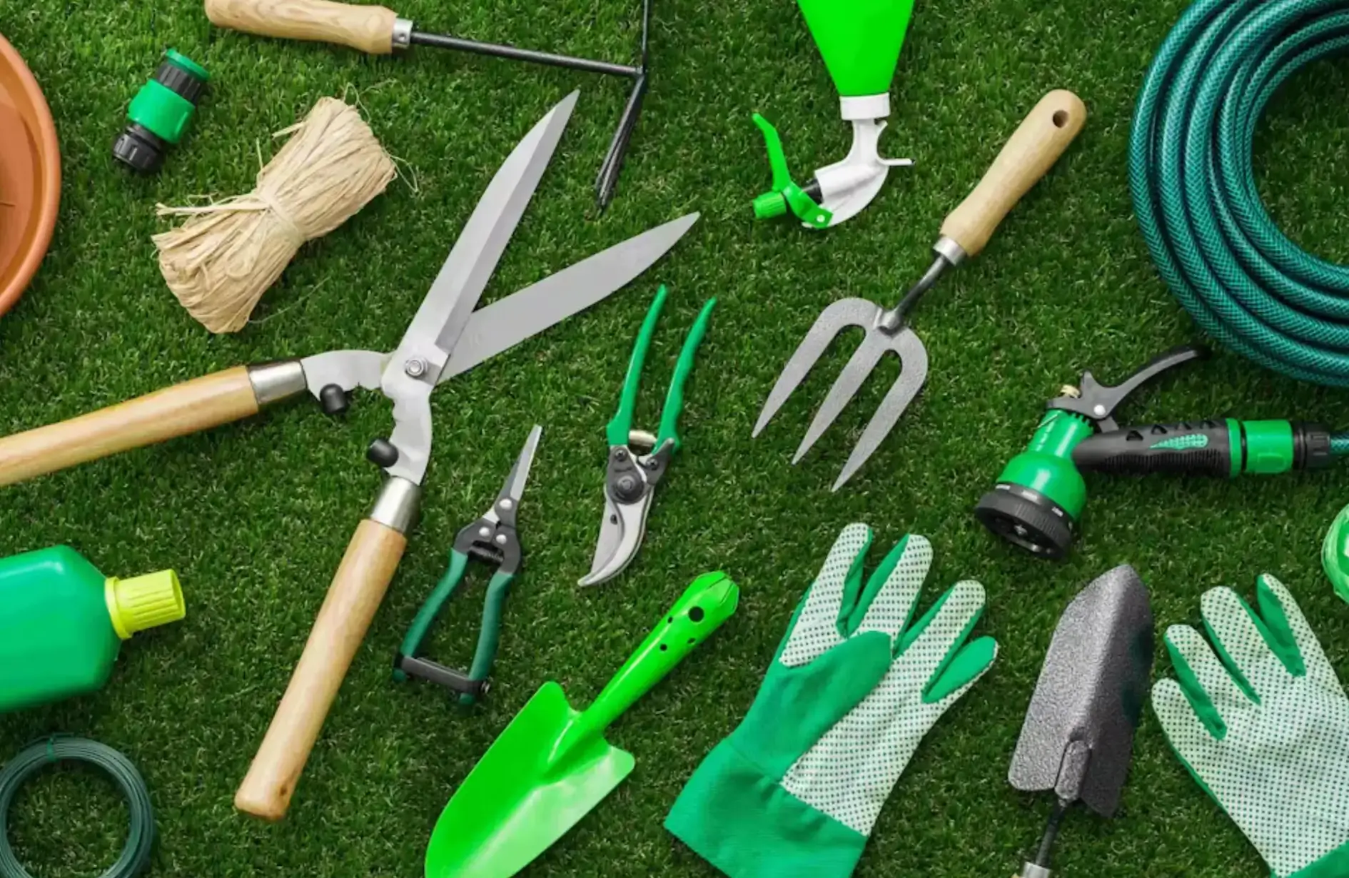 Essential lawn maintenance tools including garden shears, trowel, hand fork, pruning shears, gloves, and a hose arranged on green grass for professional Edmonton landscaping services.