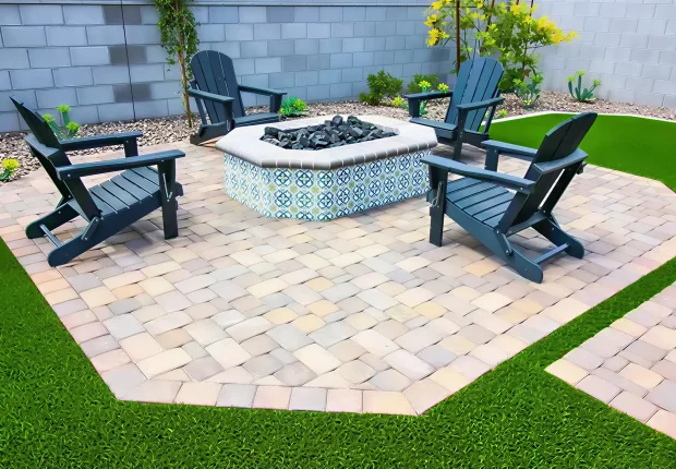 Custom residential patio design in Edmonton featuring interlock patio stones, a decorative tiled fire pit, and dark Adirondack chairs on a manicured lawn.