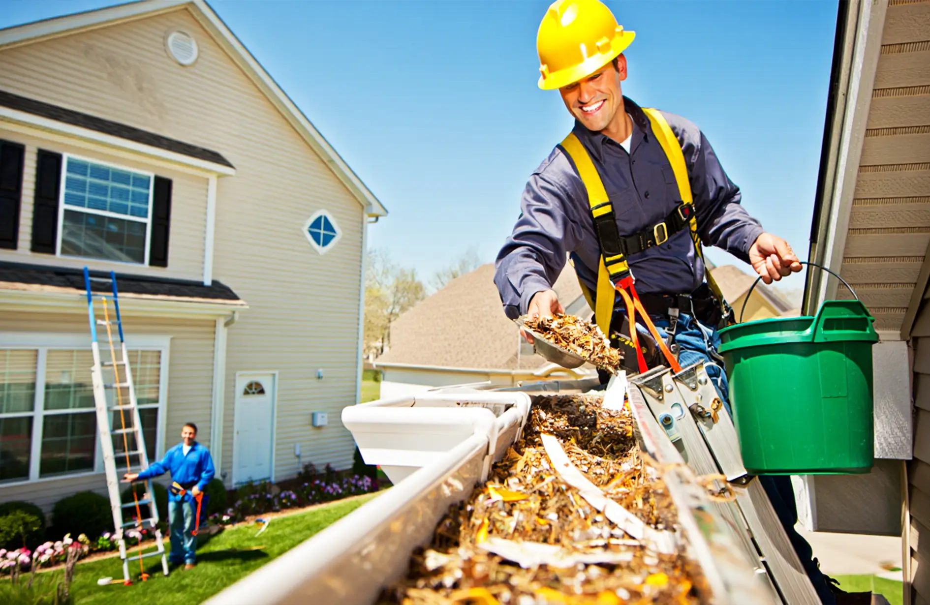 Professional worker in safety gear cleaning debris and leaves from a house gutter into a bucket.