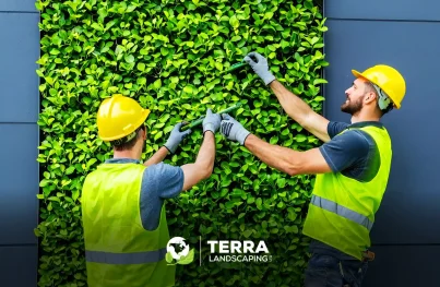 Two professional landscaping workers in safety vests and hard hats maintaining a lush green living wall installation in edmonton.